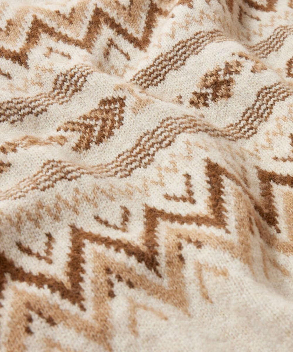 Close-up of a knitted textile with a geometric zigzag pattern in warm brown and beige