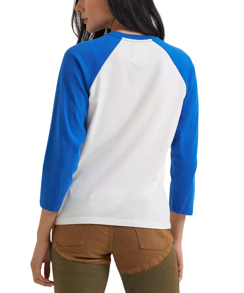 A woman shown from the back wearing a colorblock raglan long-sleeve shirt with a white back panel, blue shoulder yokes, and brown pants against a plain white background.