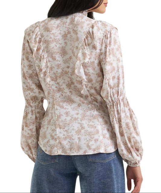 A woman shown from the back wearing a long-sleeve blouse with a beige and brown floral pattern featuring subtle western motifs on the white blouse, gathered ruffles at the shoulders, and elasticized cuffs