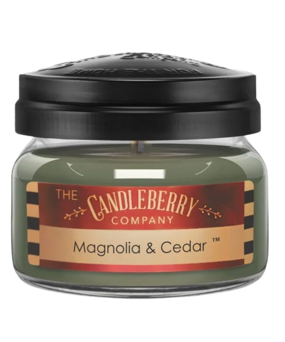 A jar candle from The Candleberry Company in the Magnolia & Cedar scent, featuring olive green wax in a clear glass jar with a black lid and a red and beige label.