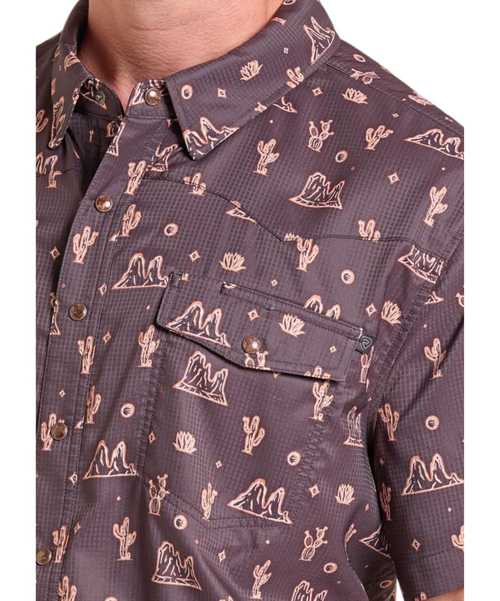Close-up view of the men's black short sleeve snap shirt featuring the beige colored desert conversational print, chest pockets with pen slot, hidden snap down collar, and western yokes