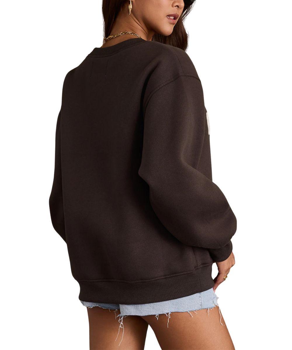 A woman wearing an oversized dark charcoal crewneck sweatshirt, shown from a side-back angle against a plain white background.