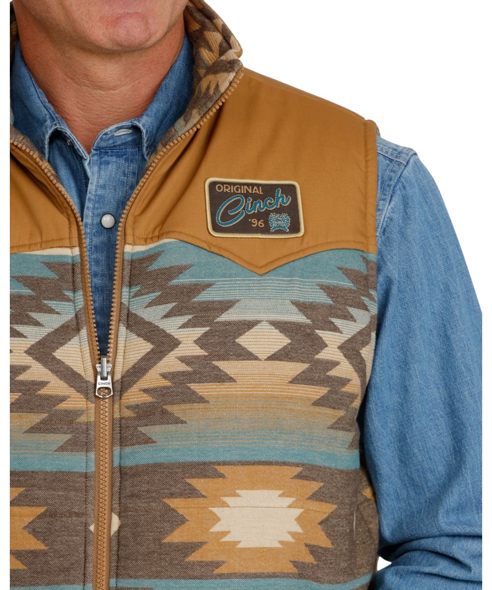 Close-up view of the men's blue serape reversible vest featuring the woven logo patch at the left chest featuring the water-resistant finish and quilted design