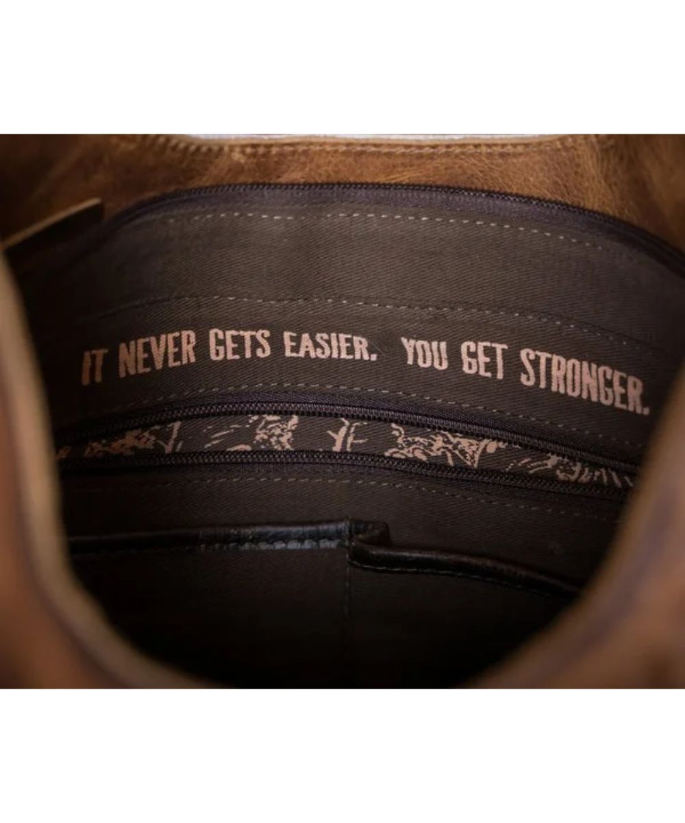 Interior view of the women's hobo bag featuring the quote inside that reads: "It Never Gets Easier. You Get Stronger.", an interior zip pocket, and 2 slip pockets