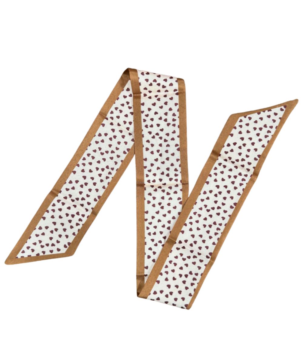 Western-inspired skinny mini scarf featuring a brown heart print on tan polyester. Cowgirl necktie can be worn as a headband, purse wrap, neckerchief, and more.