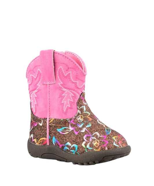 A toddler's western-style boot featuring a bright pink faux-suede shaft with embroidered stitching, a glittery brown footbed decorated with a colorful floral pattern, and a dark brown sole.
