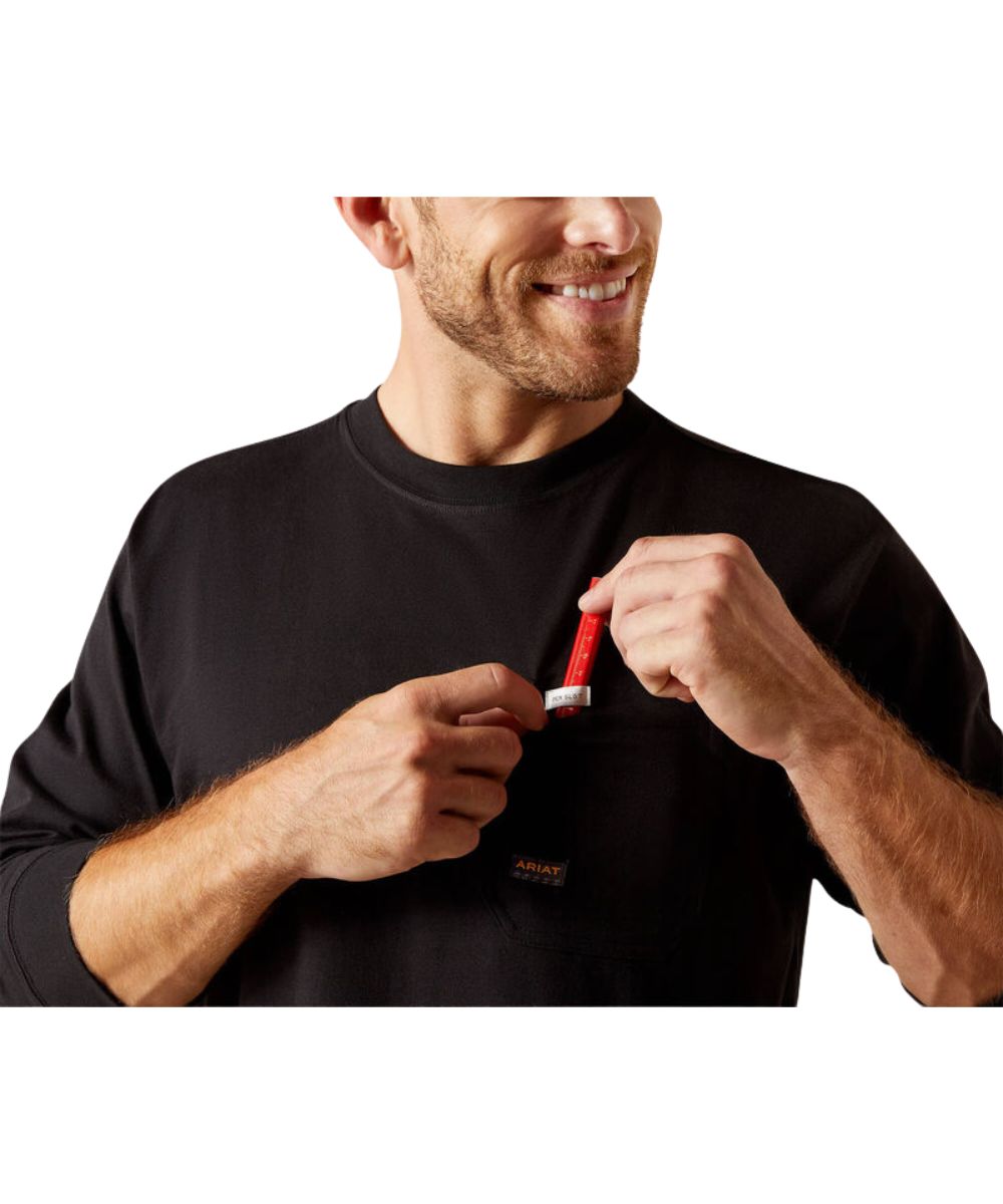 A man wearing a black long-sleeve crewneck shirt with a small chest pocket, shown from the chest up against a white background. He is smiling and holding a carpenter's pencil near the pocket.