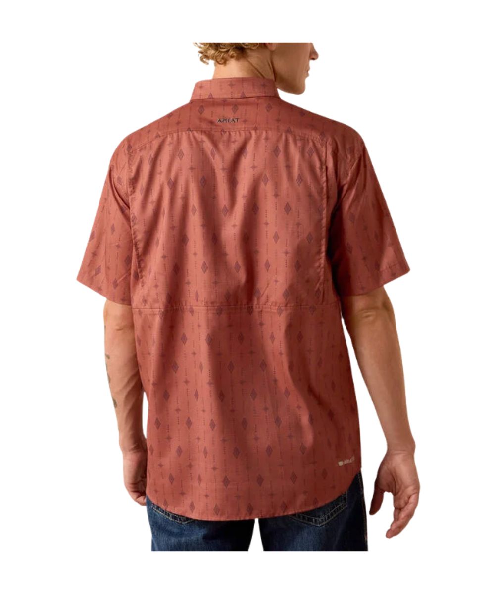 A man wearing a short-sleeve button-up shirt by Ariat, shown from the back. The shirt is a dusty terracotta or rust color with a subtle dark geometric pattern.