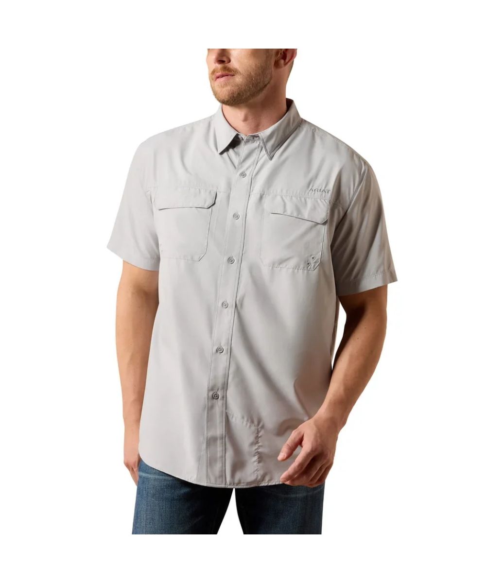 A man wearing a light gray short-sleeve button-up shirt with two chest pockets, paired with blue jeans, shown against a plain white background.