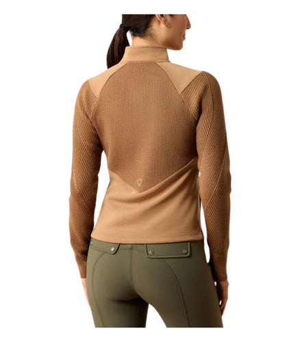 A woman shown from the back wearing a tan ribbed mock-neck long-sleeve top with contrasting beige shoulder panels and olive green riding pants, against a plain white background.