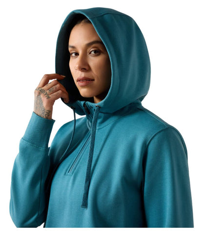 A woman wearing a teal blue pullover hoodie with a half-zip neckline and drawstrings, shown against a plain white background.