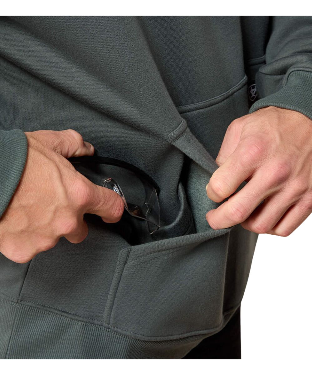 Close-up of a person wearing a dark gray hoodie and pulling a black pocket watch out of the front pocket.