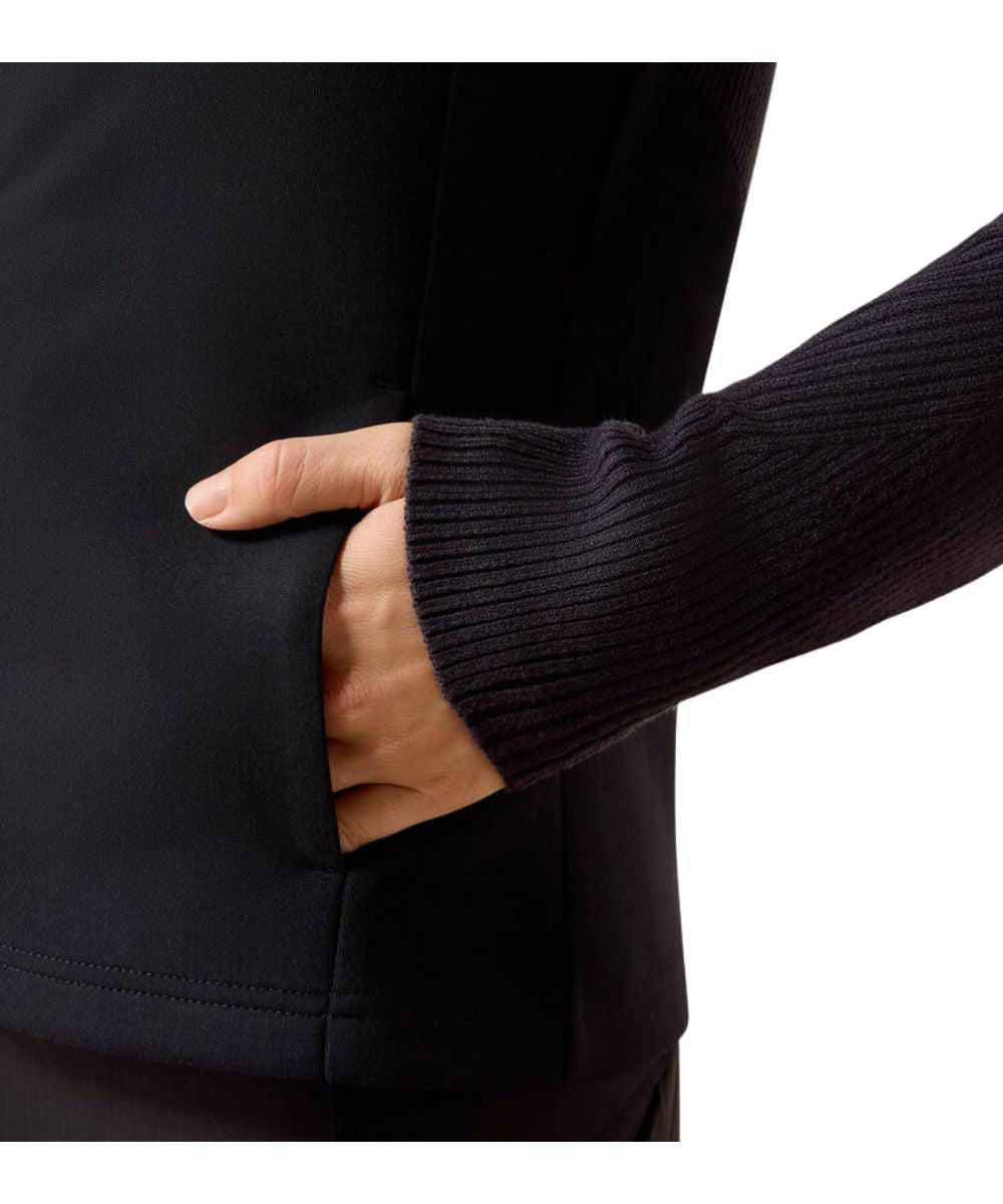 Close-up of a person wearing a navy jacket with a side pocket, showing a hand reaching into the pocket and a ribbed navy sleeve.