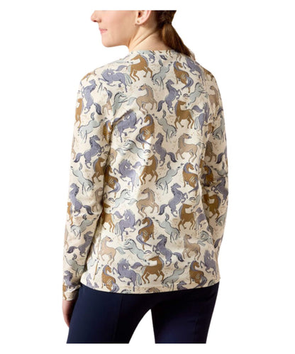 A woman shown from the back wearing a long-sleeve cream-colored shirt with an all-over repeating pattern of horses in brown, blue-gray, and beige, paired with dark navy pants against a plain white background.