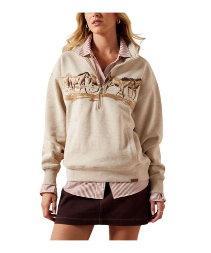 A woman models a beige quarter-zip pullover sweater featuring a graphic print of horses across the chest, layered over a pink and white striped collared shirt and a dark brown mini skirt, against a plain white background.