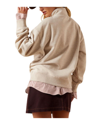 A woman shown from the back wearing a beige mock-neck knit sweater over a pink and white striped ruffled shirt and a dark brown skirt, against a plain white background.