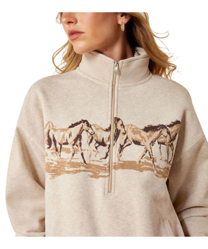 A woman wearing a light beige heathered quarter-zip sweatshirt with a graphic print of running horses across the chest.