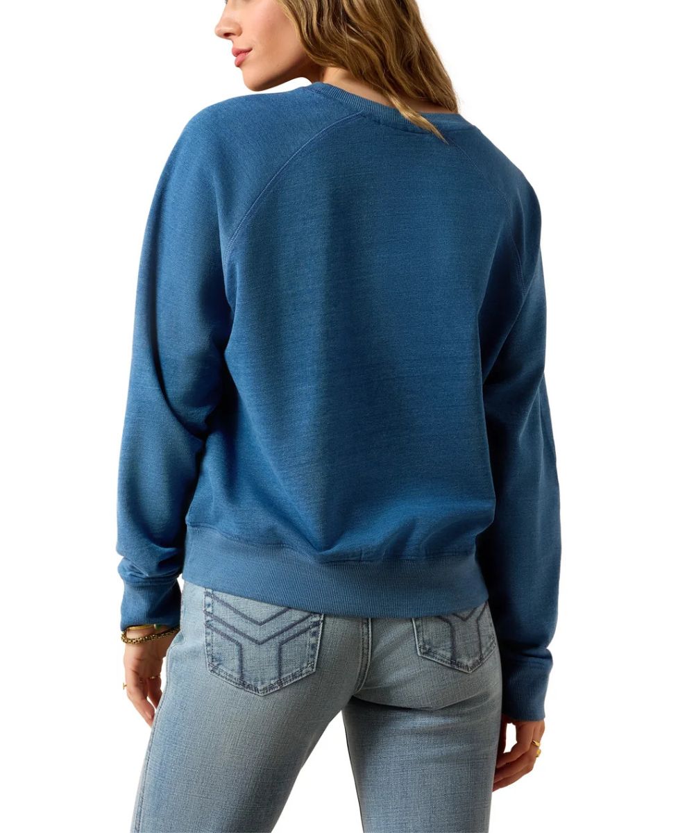 A woman shown from the back wearing a blue long-sleeve crewneck sweatshirt and light-wash jeans against a plain white background.