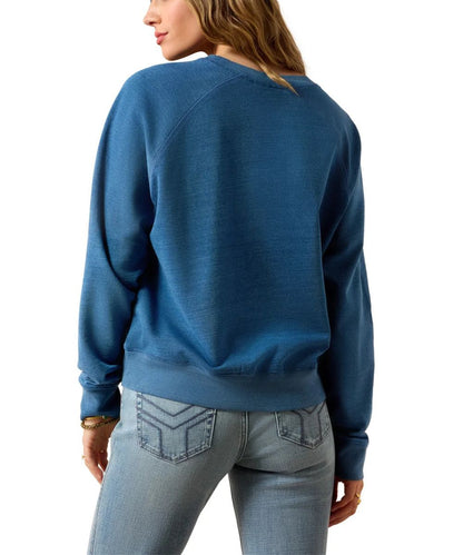 A woman shown from the back wearing a blue long-sleeve crewneck sweatshirt and light-wash jeans against a plain white background.