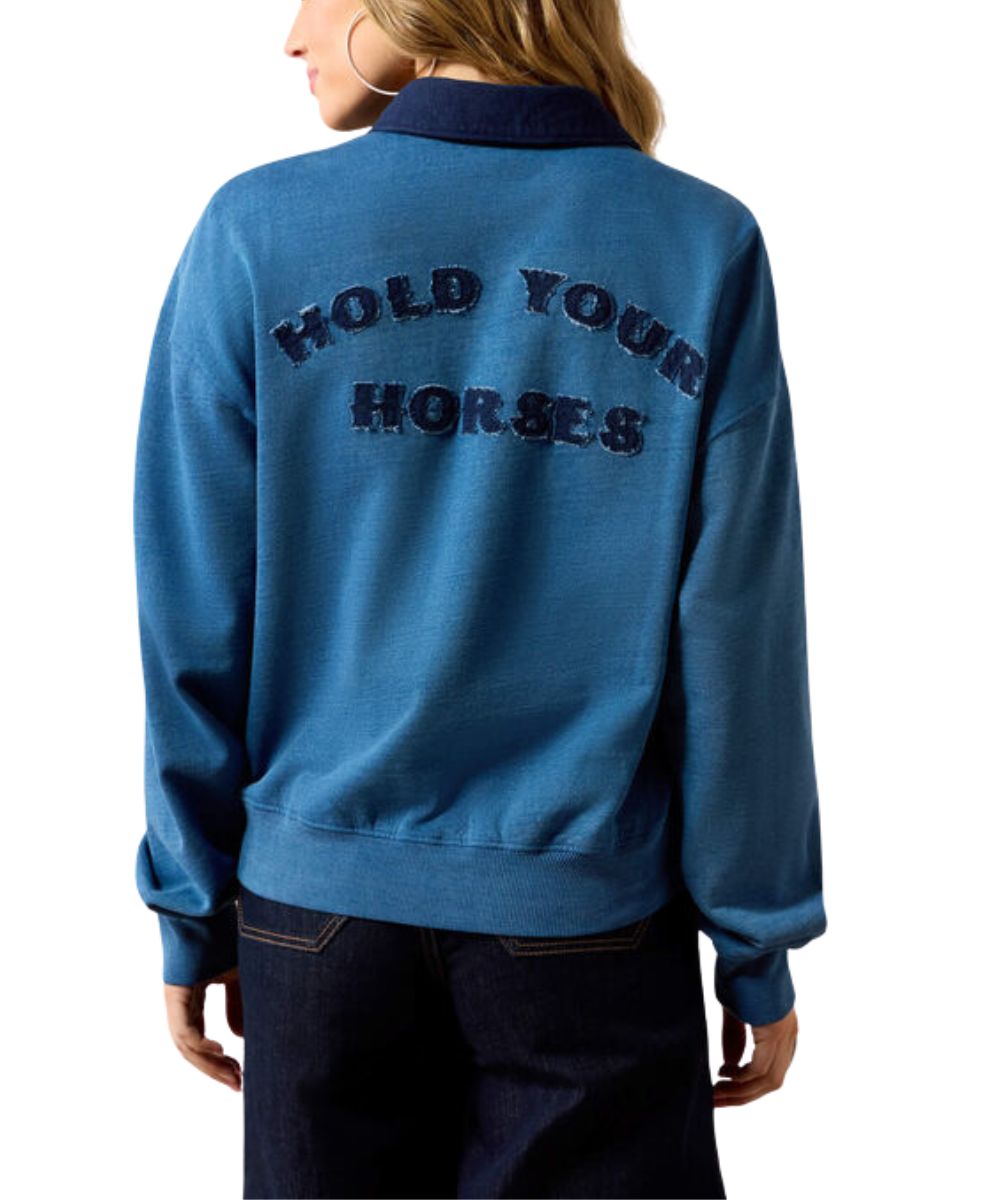 A woman shown from the back wearing a blue long-sleeve sweatshirt with 'HOLD YOUR HORSES' embroidered in dark blue across the upper back, paired with dark jeans against a plain white background.