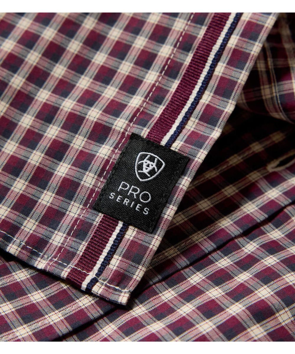 Close-up of a plaid shirt placket showing a black fabric label with the embroidered shield logo and text 'PRO SERIES'. The plaid pattern features burgundy, navy blue, and cream stripes.