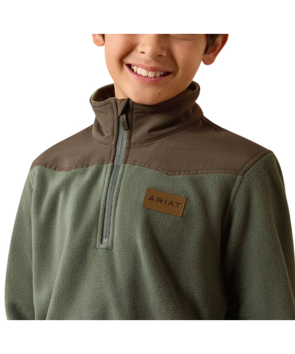 A child wearing an olive green and brown quarter-zip fleece pullover with a brown 'ARIAT' logo patch on the chest, shown against a plain white background.