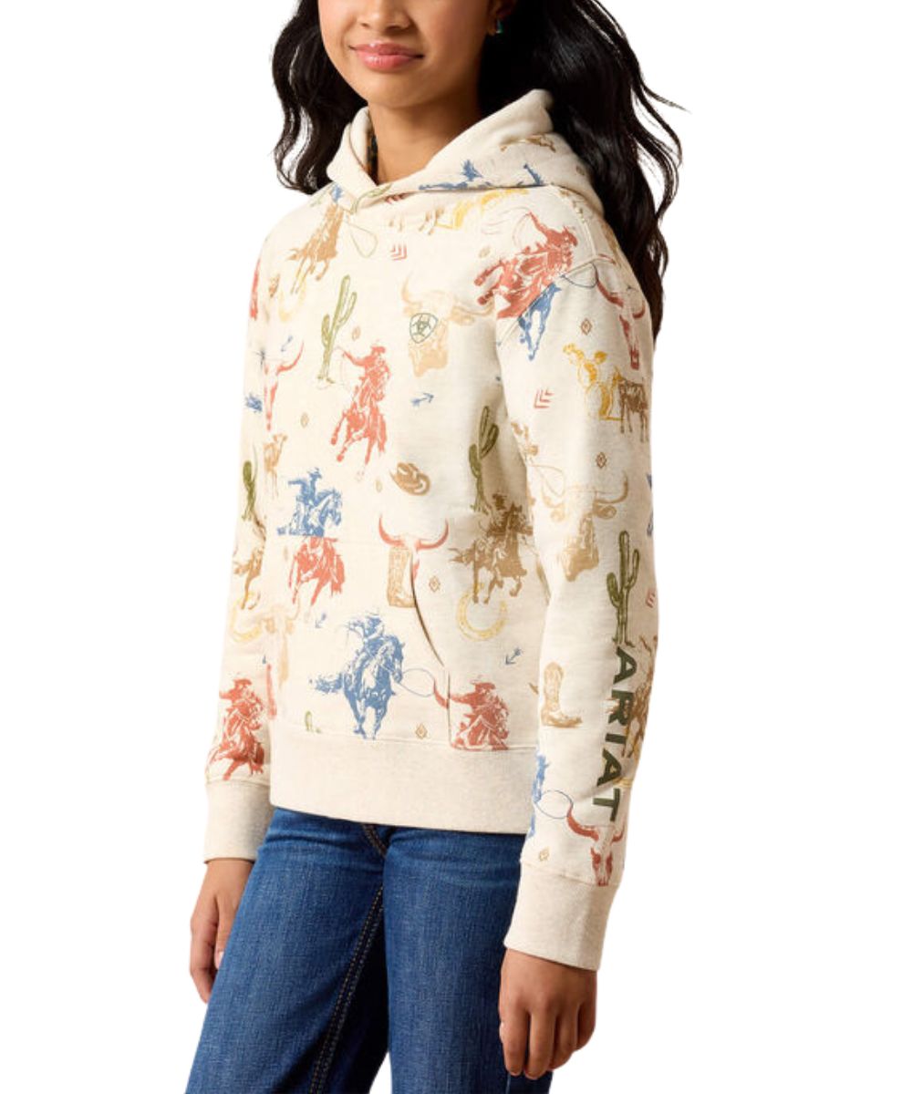 A woman wearing a cream-colored hoodie with a colorful western-themed knit pattern featuring cacti, longhorns, and riders, paired with blue jeans against a white background.