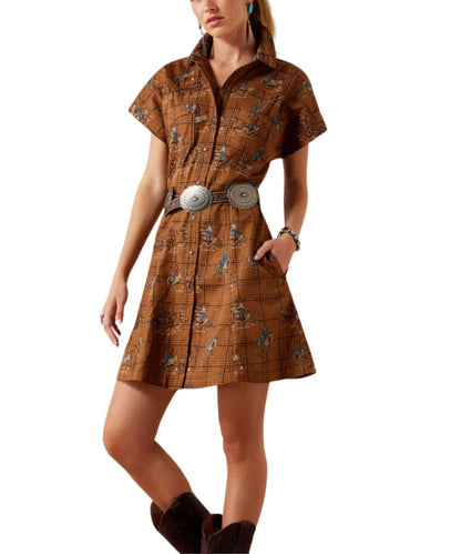 A woman models a brown short-sleeve collared shirt dress with a western-style plaid pattern and a wide belt with large silver conchos, set against a plain white background.