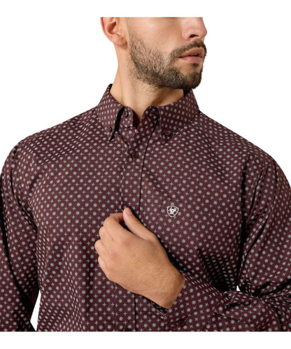 A man wearing a dark burgundy long-sleeve button-down shirt with a small white geometric pattern and a small shield logo on the chest, shown against a plain white background.