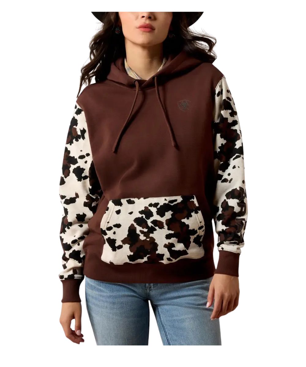 A woman wearing a brown and cow-print hoodie with blue jeans, shown from the waist up against a plain white background.