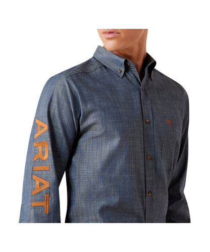Close-up view of the men's chambray blue long sleeve button down shirt featuring the single open chest pocket with a hidden pen/pencil slot, saddle brown logo embroidery, and button down collar