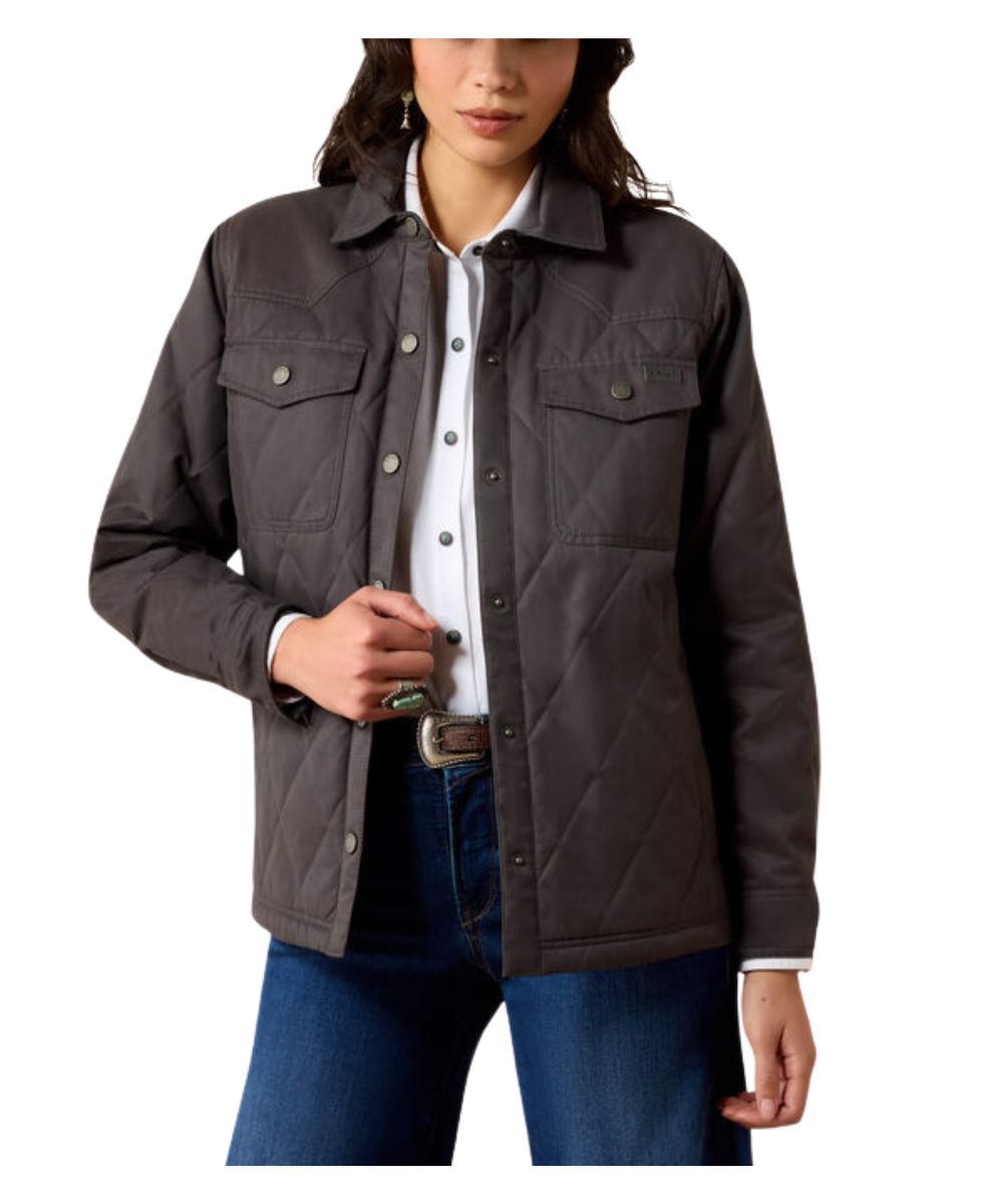 A woman wearing a dark brown diamond-quilted button-up jacket over a white collared shirt and blue jeans, shown from the waist up against a plain white background.