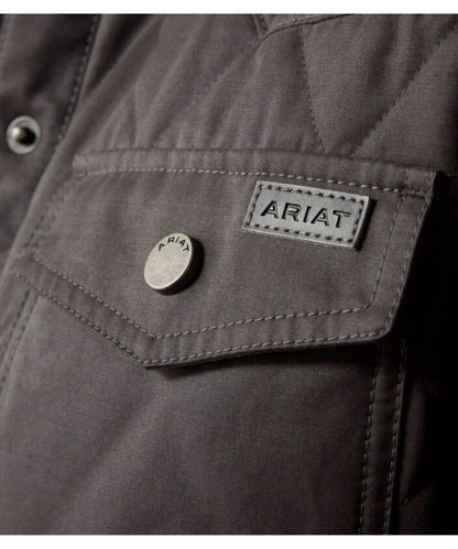 Close-up of a dark gray quilted jacket pocket with a silver button and a rectangular Ariat brand patch.
