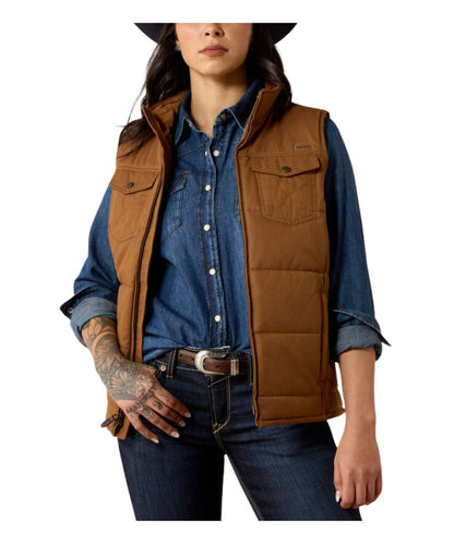 A woman wearing a brown quilted puffer vest over a blue denim shirt and jeans, shown from the chest down against a plain white background.