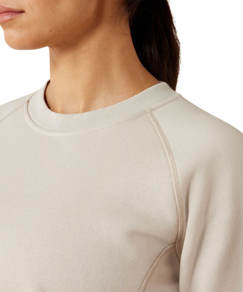 Close-up of a person wearing a light beige crewneck sweatshirt, showing the ribbed collar, shoulder seam, and smooth fabric texture against a plain white background.