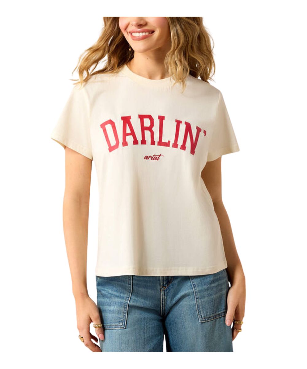 A woman wearing a cream-colored short-sleeve t-shirt with 'DARLIN'' printed in red across the chest, paired with blue jeans, against a plain white background.