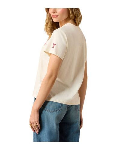 A woman shown from the back wearing a cream-colored short-sleeve t-shirt with a small red embroidered ribbon on the left shoulder, paired with blue jeans, against a plain white background.