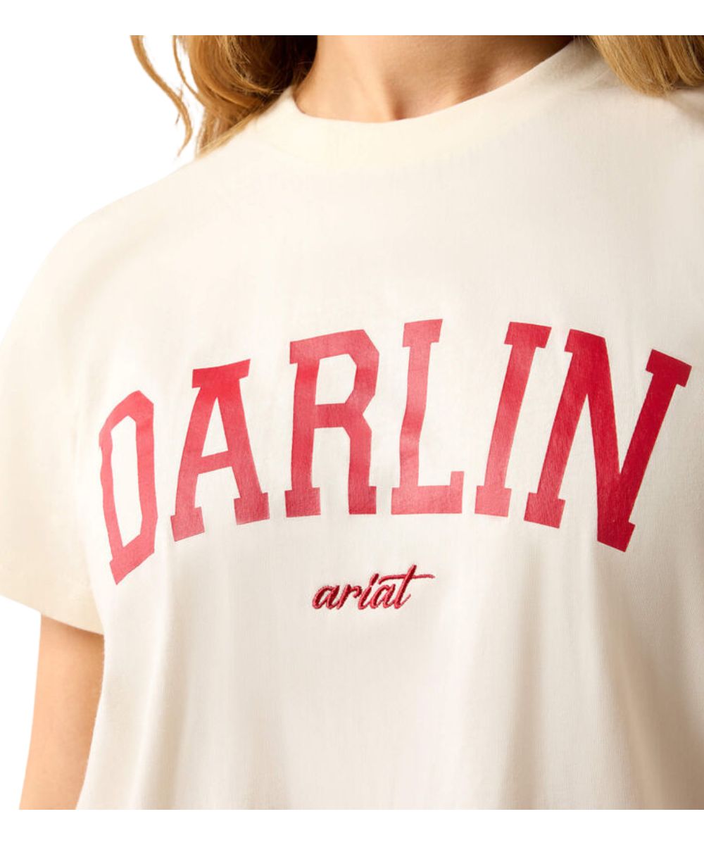 A close-up of a person wearing a cream-colored t-shirt with 'DARLIN' printed in large red varsity letters and 'ariat' in red script underneath.