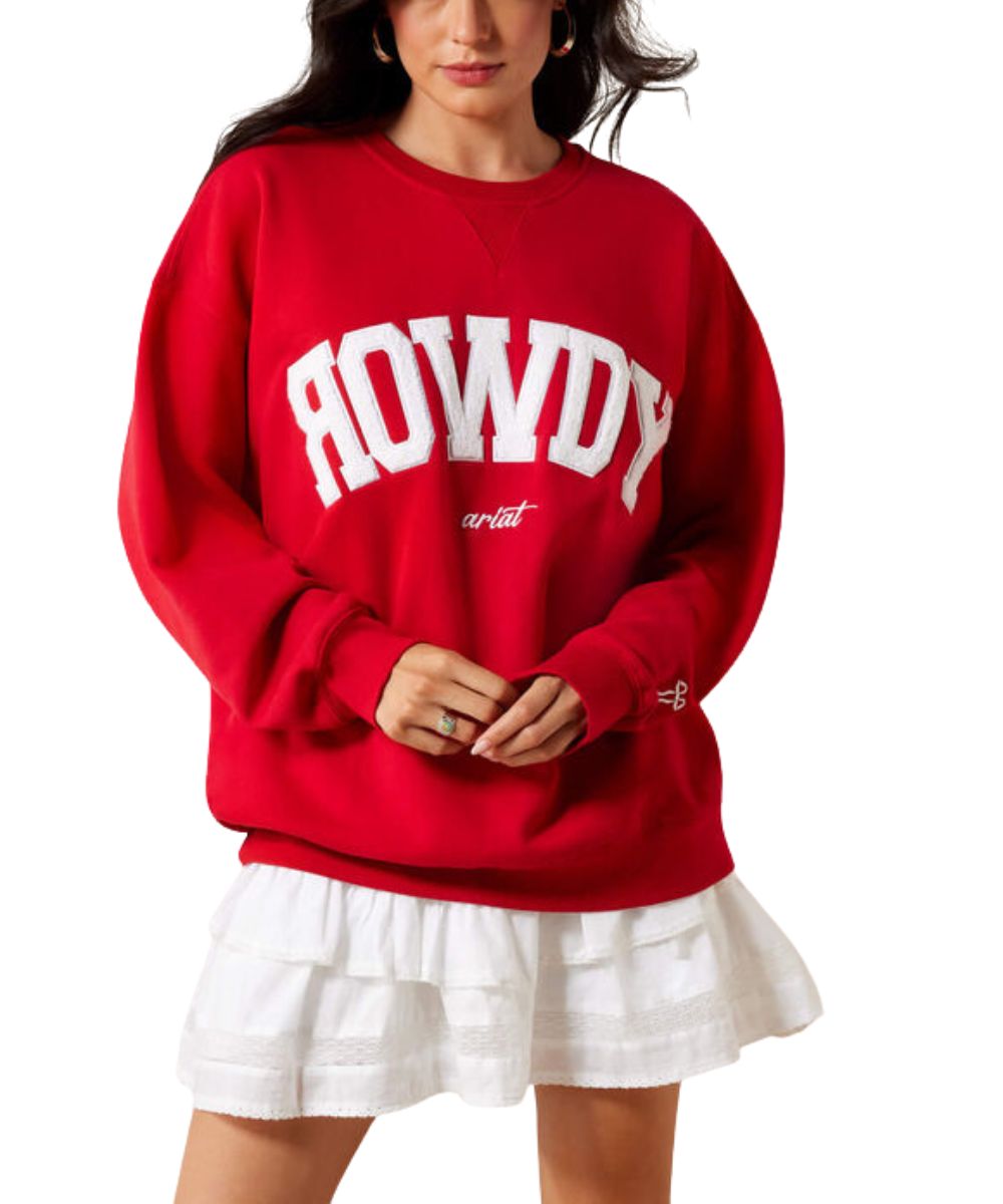 A woman wearing a red crewneck sweatshirt with 'ROWDY' in large white varsity letters and 'artist' in smaller script, paired with a white ruffled skirt, against a plain white background.