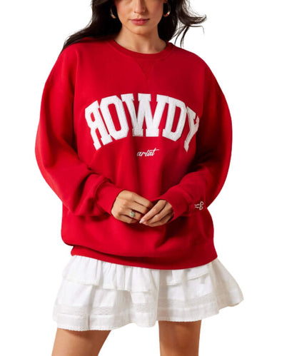 A woman wearing a red crewneck sweatshirt with 'ROWDY' in large white varsity letters and 'artist' in smaller script, paired with a white ruffled skirt, against a plain white background.