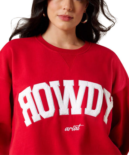 A close-up of a woman wearing a bright red crewneck sweatshirt with 'ROWDY' printed in large white arched letters across the chest and 'ariat' in smaller white script below.