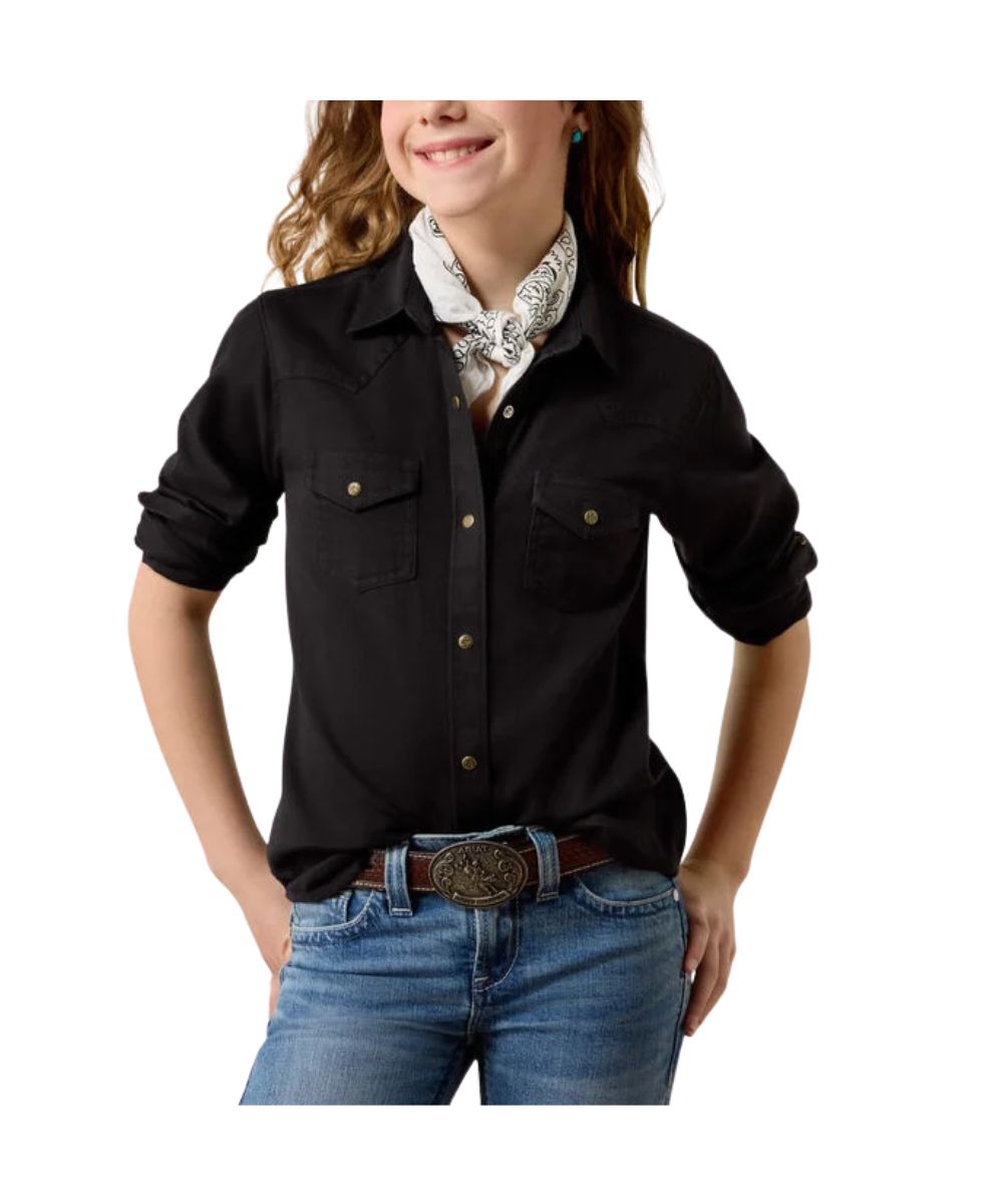 A girl wearing a black western-style button-up shirt with rolled sleeves, two chest pockets, and gold-tone snaps, paired with blue jeans and a white patterned neck scarf, against a plain white background.