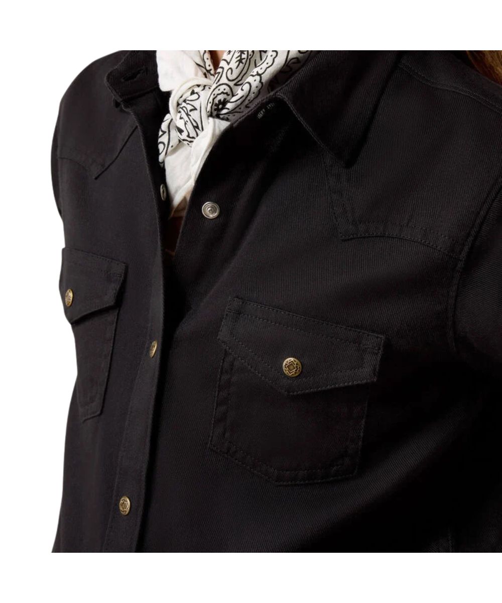 Close-up of a black western-style button-up shirt with chest pockets and gold-tone snap buttons, worn over a white paisley neck scarf.