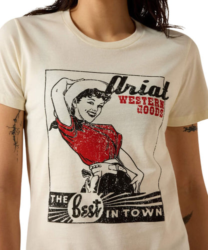 A close-up of a person wearing a cream-colored graphic t-shirt. The shirt features a vintage-style distressed print of a woman in a cowboy hat and red top, with text reading 'Ariat Western Goods' and 'The best in town'.
