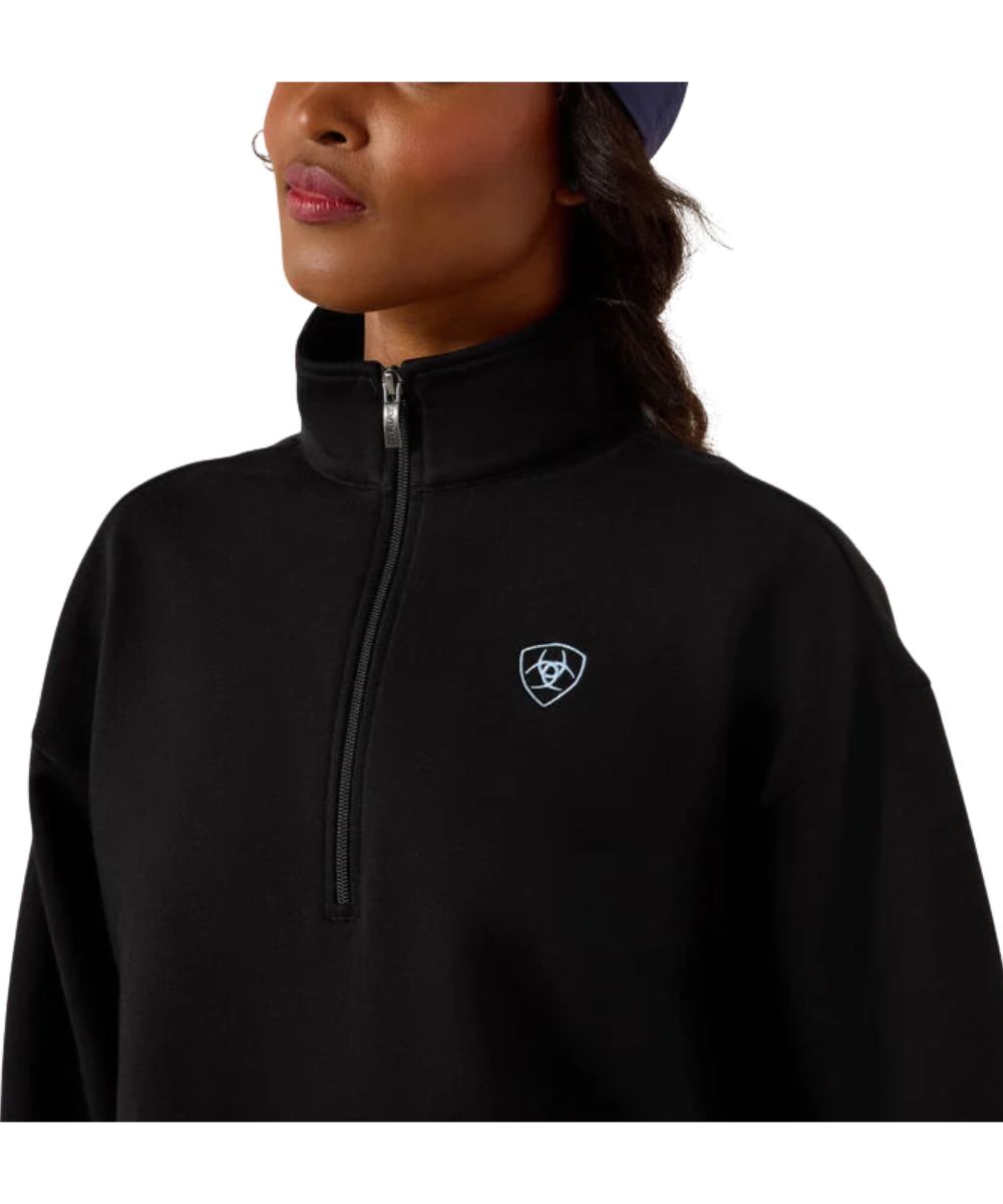 Woman wearing a black half zip sweatshirt with an Ariat logo on the left chest