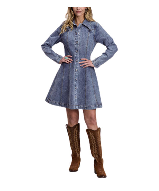 A woman modeling a blue denim long-sleeve button-front dress with a flared skirt, paired with brown cowboy boots, against a plain white background.
