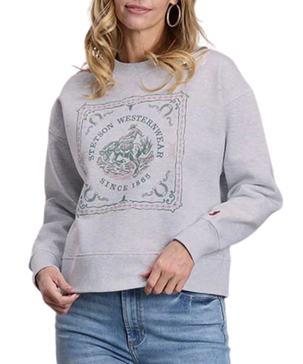 Front view of the women's heather grey Stetson long sleeve sweatshirt featuring the crew neck, dropped shoulders, and a square cowboy graphic screen-printed on the front that reads: "Stetson Westernwear Since 1865" with horseshoe corners