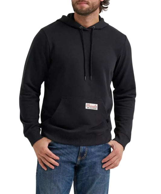 A man wearing a black pullover hoodie with a kangaroo pocket and a small rectangular logo patch on the front, paired with blue jeans against a plain white background.