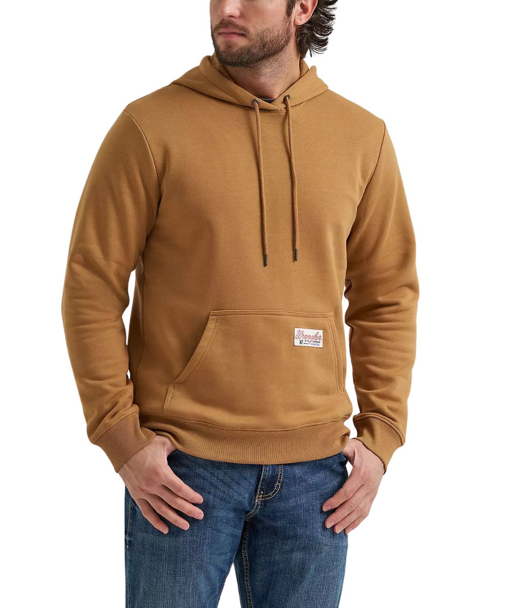 A man wearing a tan pullover hoodie with a kangaroo pocket and drawstrings, paired with blue jeans, against a plain white background.