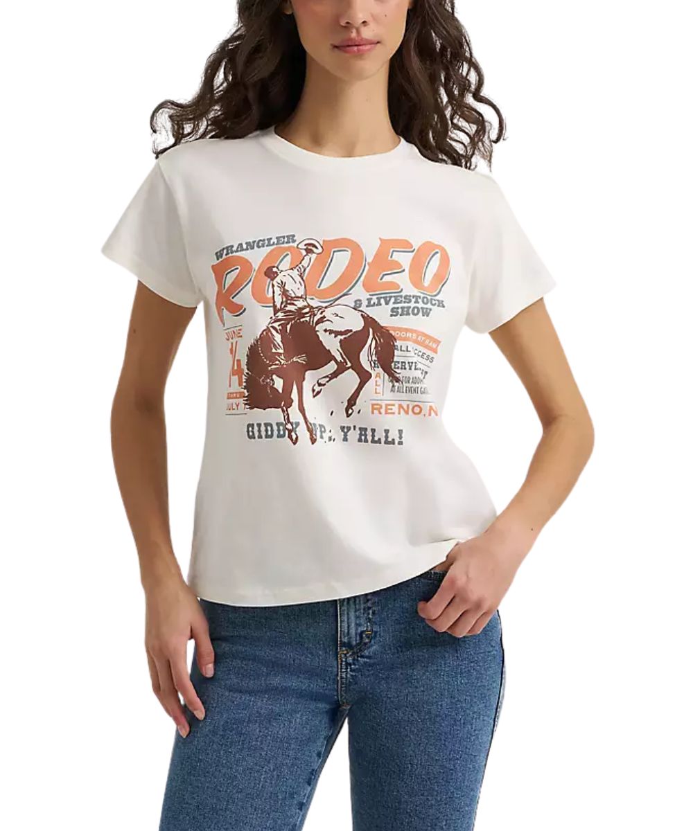A woman wearing a white Wrangler short-sleeve t-shirt with a vintage-style orange and brown 'Rodeo' graphic, paired with blue jeans, against a plain white background.